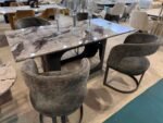 Grey marble dining table with four quilted velvet cantilever chairs in a modern showroom setting.