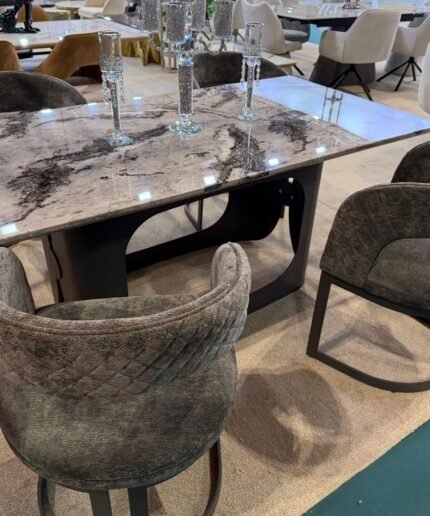 Grey marble dining table with four quilted velvet cantilever chairs in a modern showroom setting.