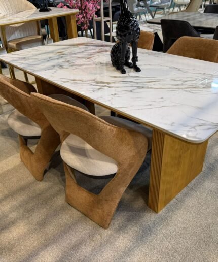 White marble dining table with gold fluted pedestal base and four tan designer chairs.